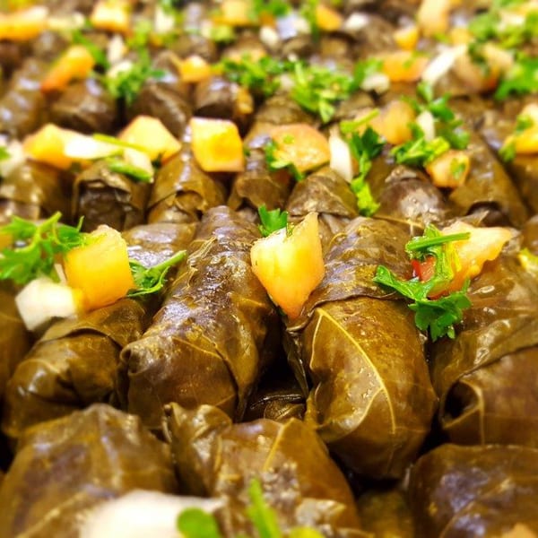 Close-up of numerous stuffed grape leaves (dolmades) garnished with diced tomatoes, onions, and parsley.