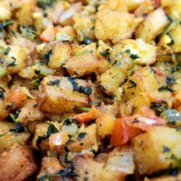 Close-up of golden-brown fried potato cubes mixed with green herbs, onions, and red bell peppers.