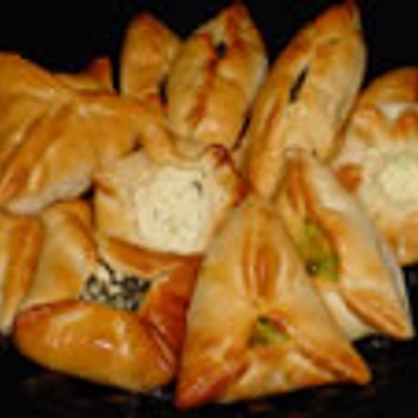 A close-up of a platter of golden-brown, triangular and star-shaped pastries with various fillings.