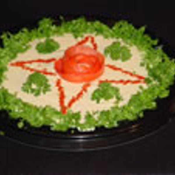 Hummus platter garnished with lettuce, tomato, parsley, and paprika, on a black plate.