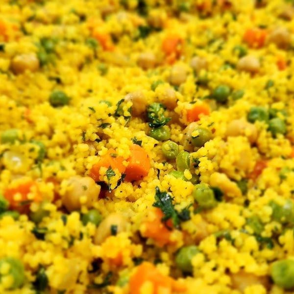 Close-up of vibrant yellow couscous with green peas, orange carrots, and chickpeas.